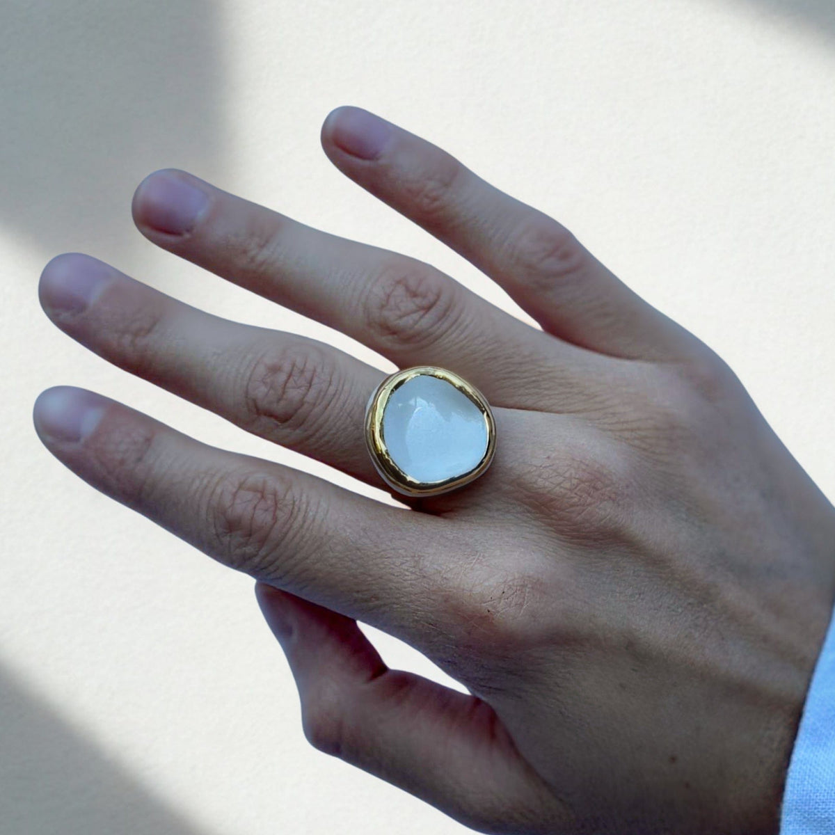 Nahaufnahme eines goldfarbenen Ringbands mit weißem Keramikelement am Finger