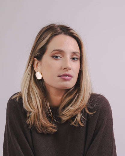 Mujer con white and gold ceramic earrings with a brown sweater against a plain background