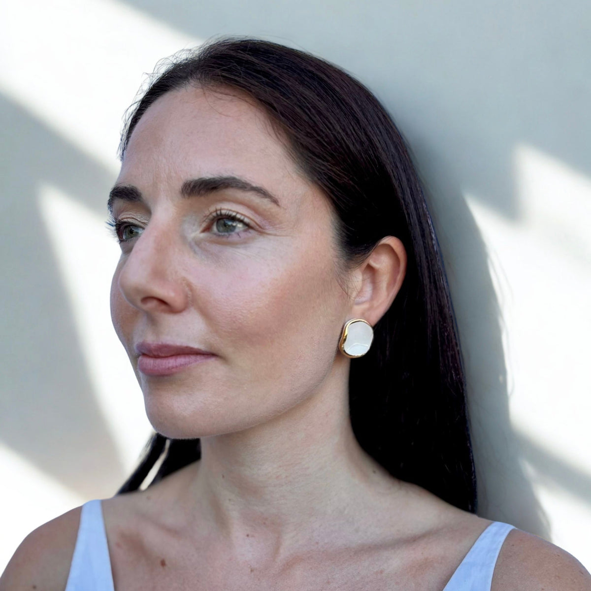 Mujer con white and gold ceramic earrings with a white top with a neutral background