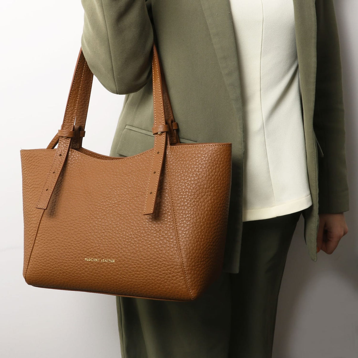 Pebbled tan leather tote with long handles carried by a person in an olive green blazer.