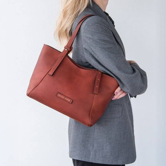 Donna con borsa Libra in pelle marrone e logo del brand visibile su sfondo chiaro