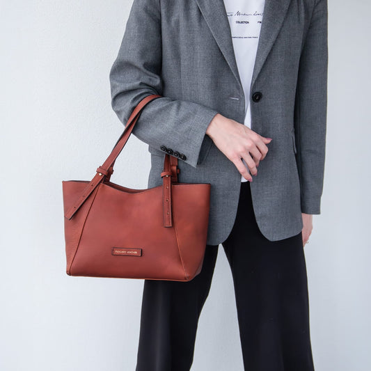 Persona tiene una borsa Libra in pelle marrone su sfondo semplice