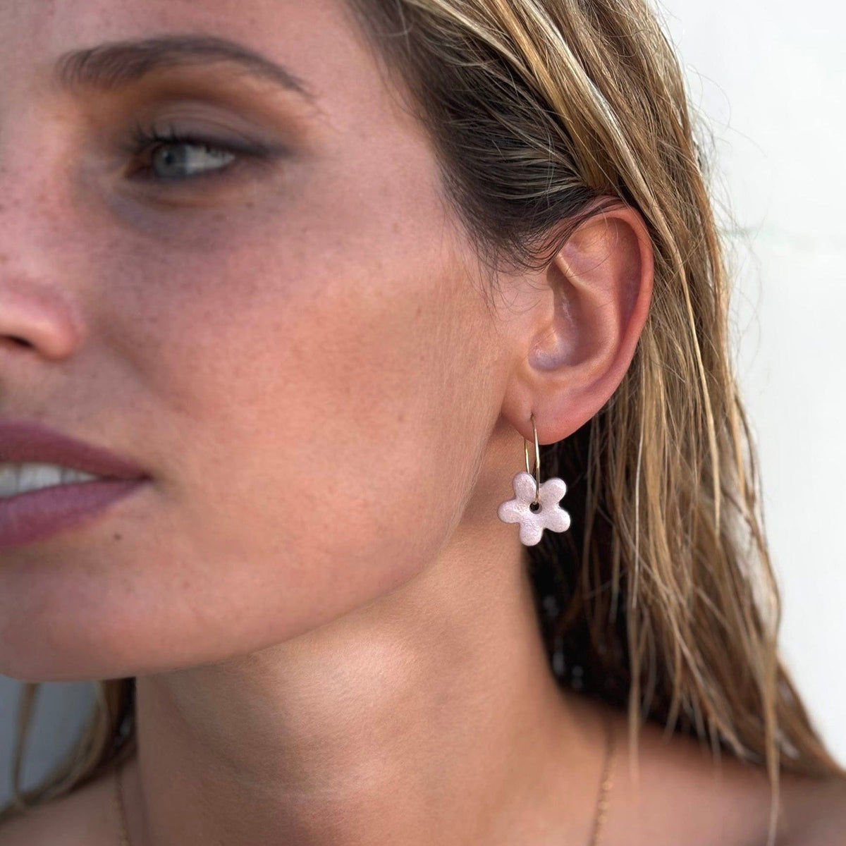 Pink floral ceramic dangle earring on a slender gold hoop worn by a model