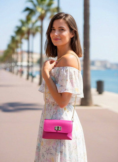 Woman in a floral dress with a pink handbag by palm trees and water.