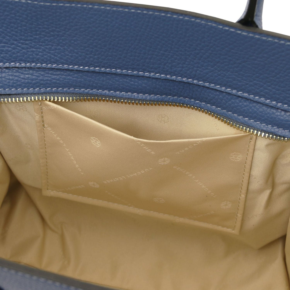 Open view of blue leather tote showing beige fabric interior pocket with subtle branding and detailed stitching inside zippered compartment.