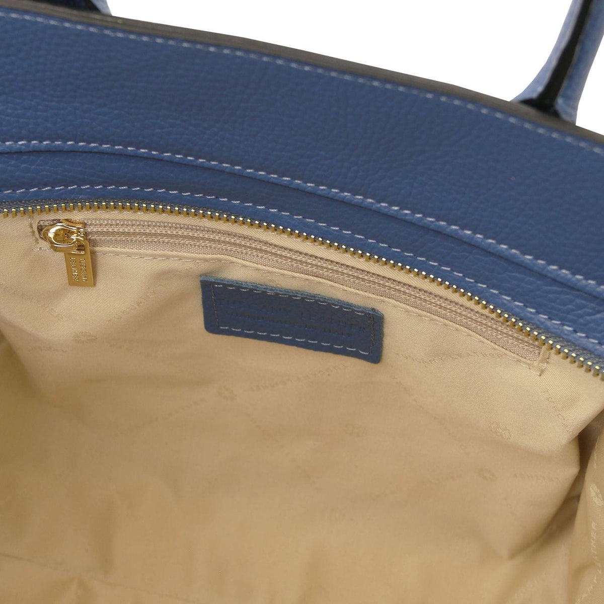 Interior view of blue Italian leather tote showing beige fabric lining, interior zip pocket with gold zipper pull, and stitched leather label.