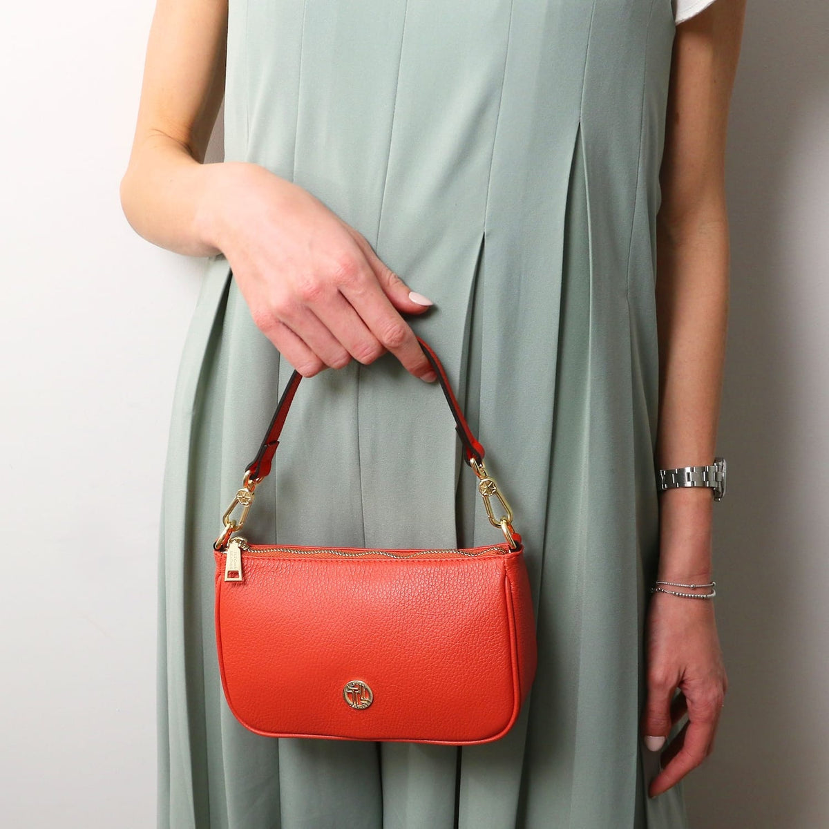 Parfait leather clutch in arancione coral con accessori metallici color oro e a rosso strap tenuta da una modella in a mint dress