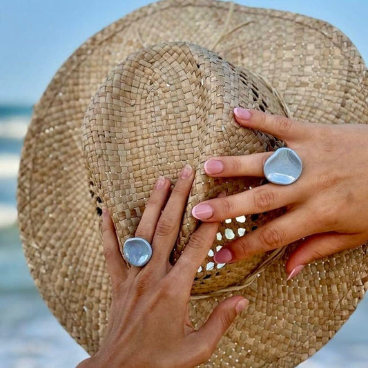 Two light blue pearl ceramic Perla rings on fingers with a woven straw hat in the background.