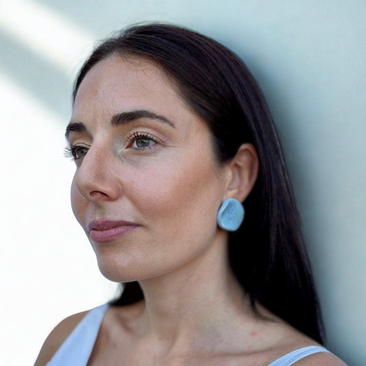 Portrait of a woman wearing a light blue ceramic pearl stud earring from the Perla collection
