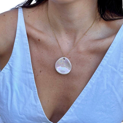 Handcrafted pearl pink ceramic pendant on a delicate gold chain worn on a light blue top