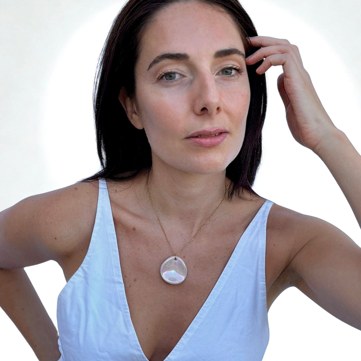 Portrait of a woman wearing a handcrafted pearl pink ceramic necklace with a round iridescent pendant on a thin gold chain