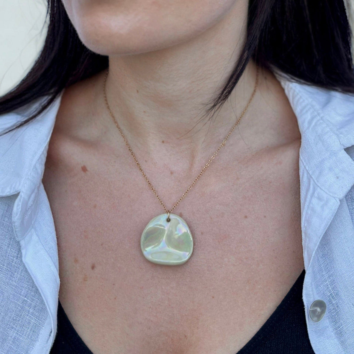 Close-up of the Perla necklace pendant in sage-green ceramic on a delicate gold chain.