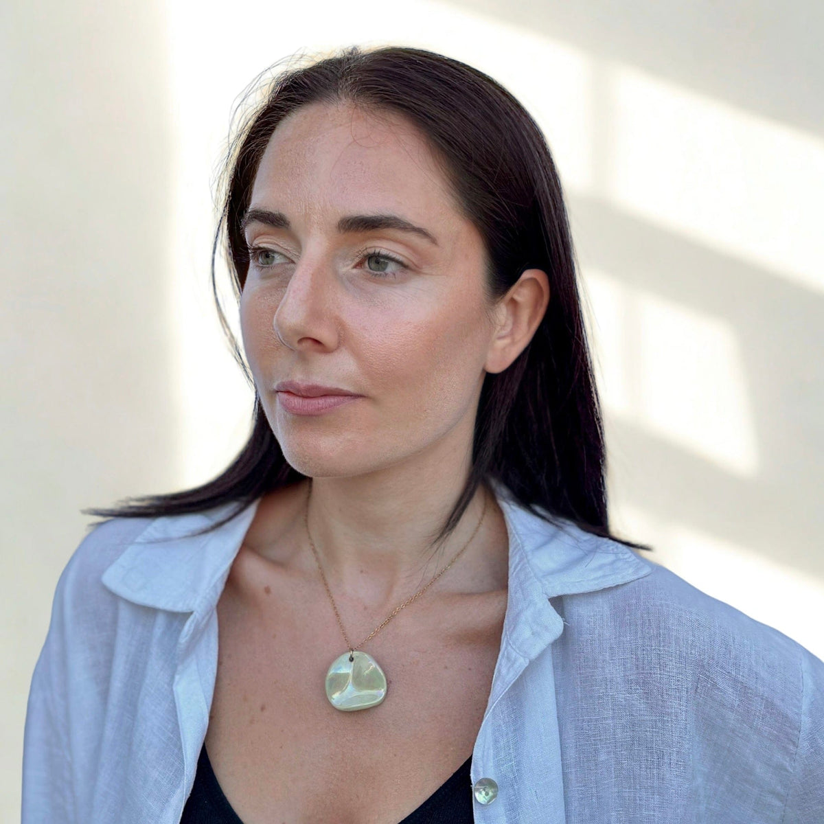 Portrait of a woman wearing the Perla sage-green ceramic pendant necklace on a gold chain.