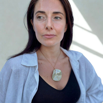 Model wearing the Perla sage-green ceramic pendant necklace over a black top with a light blue shirt.