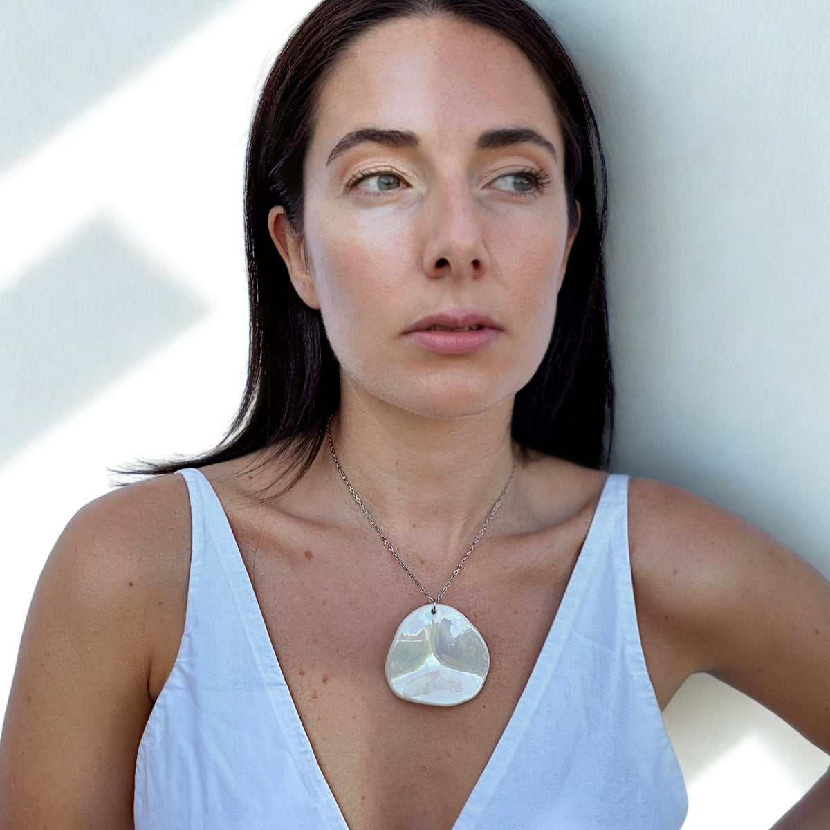 Woman wearing a large pearl-white handcrafted ceramic necklace from the Perla collection.