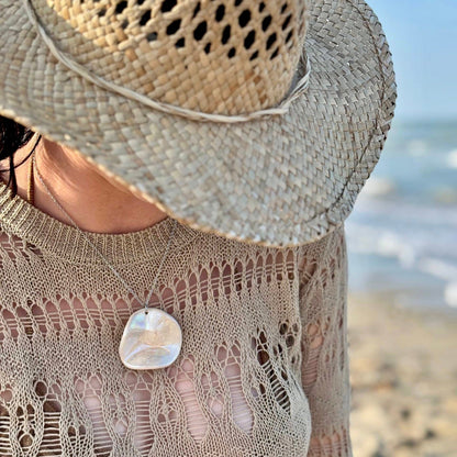 Woman wearing the pearl-white ceramic pendant necklace at the beach with a wide straw hat.