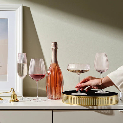Two dusty rose white wine glasses beside a champagne bottle on a white sideboard