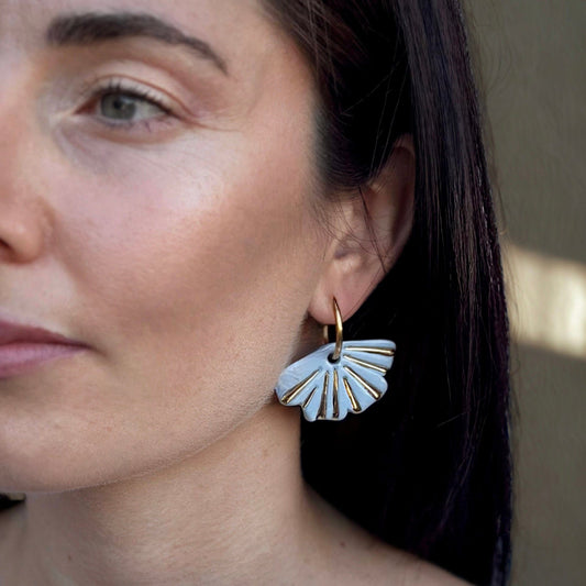 Woman wearing light blue fan shaped ceramic earrings with gold detailing