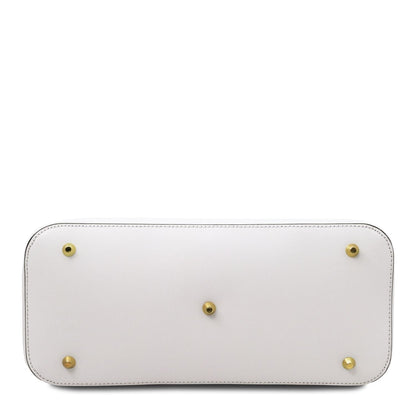 Bottom view of a white leather handbag with five brass protective feet and detailed stitching along the edges.
