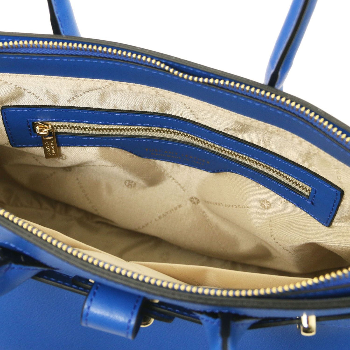Open top view of blue leather handbag revealing beige interior lining with zippered pocket and gold-tone zipper pull.