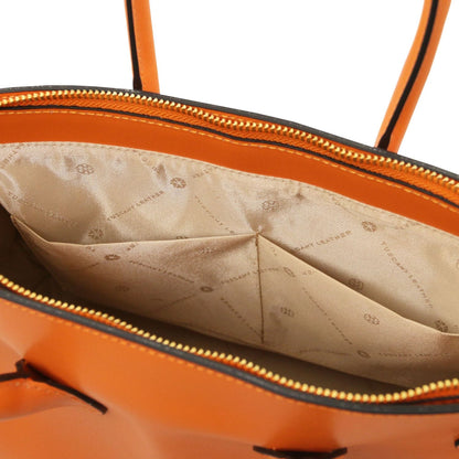 Close-up of an orange leather handbag interior showing beige fabric lining with printed logo pattern and zippered opening.