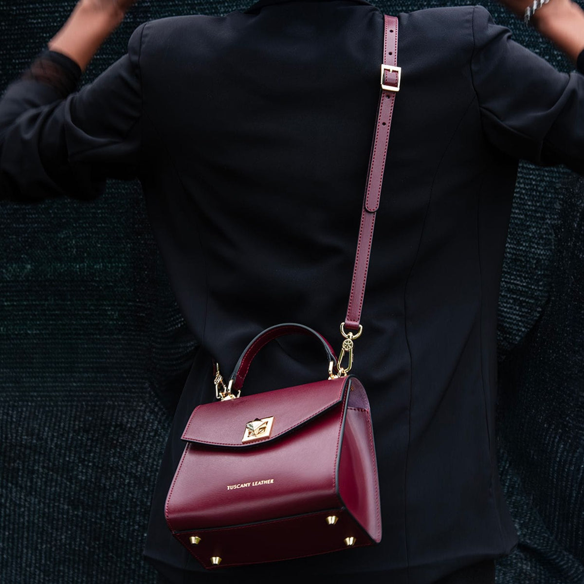 burgundy leather TL Bag mini bolso with herrajes dorados and a long strap worn over a black coat