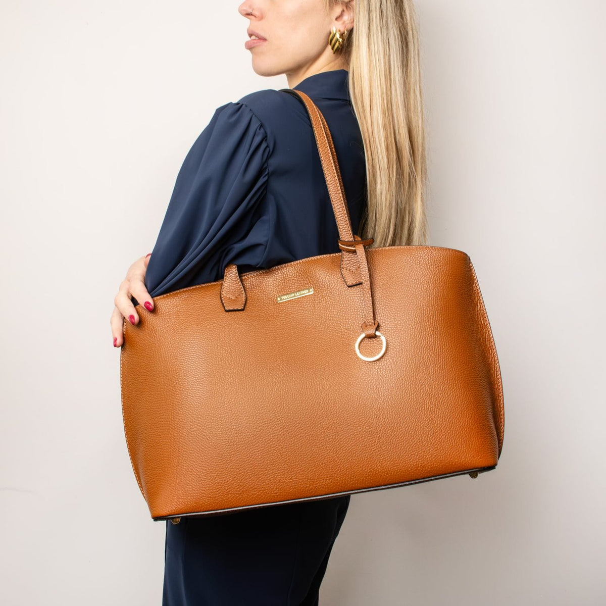 Tan pebbled leather shopping tote carried over the shoulder by a model in a navy blouse