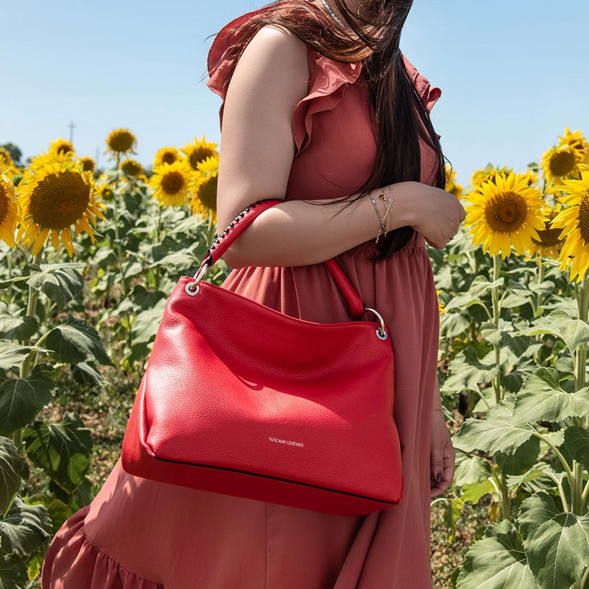 Model in a pink dress carries a red TL Bag through a sunflower field