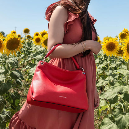 Red soft Italian leather shoulder bag with silver ring hardware carried by a woman in a sunflower field.