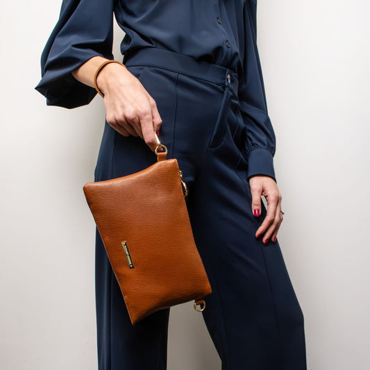 Tan pebbled leather pouch clutch held by a model wearing a navy blue tailored outfit.