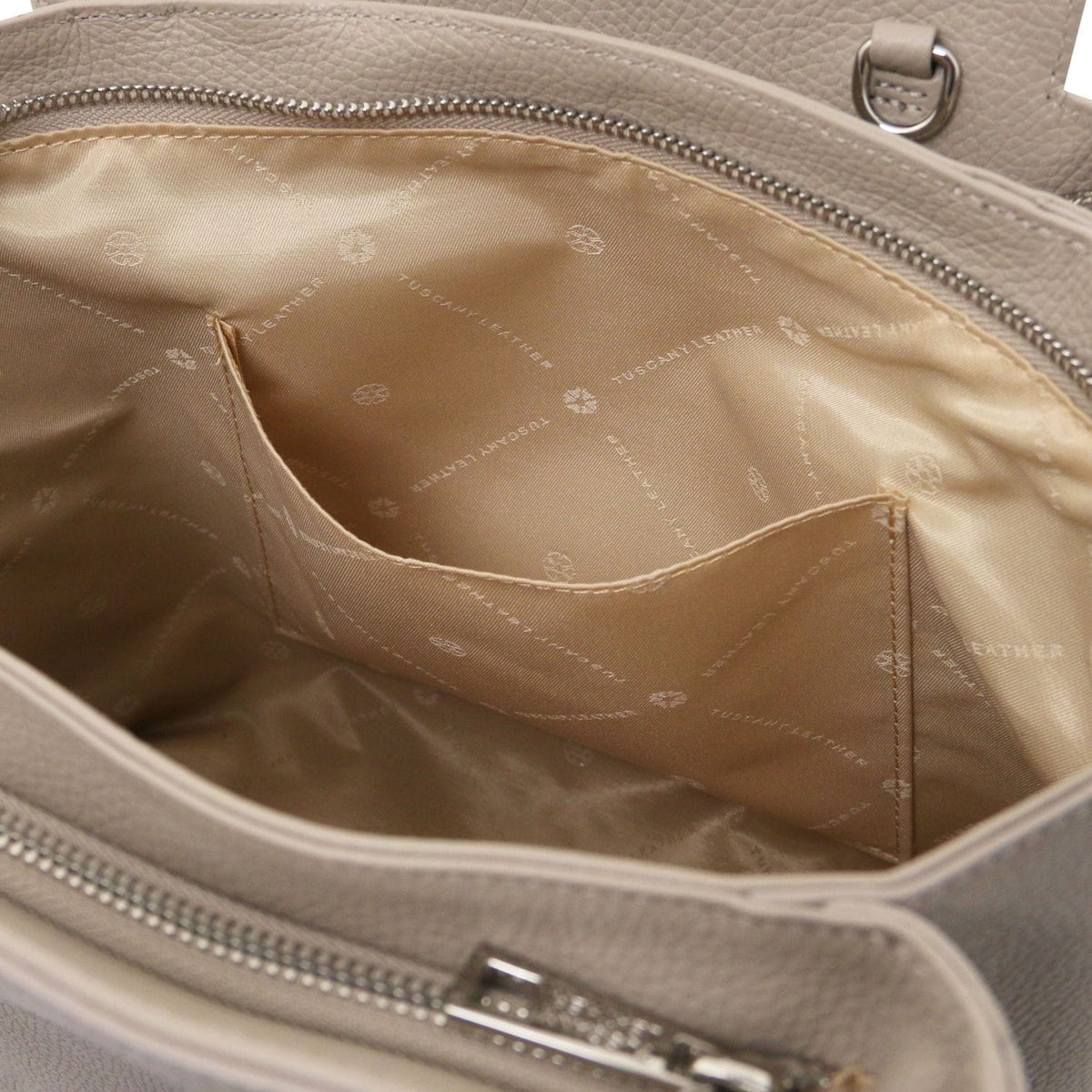 Primo piano of beige Borsa in pelle italiana interior showing silk fodera in tessuto e internal tasca aperta con zip closure edge.