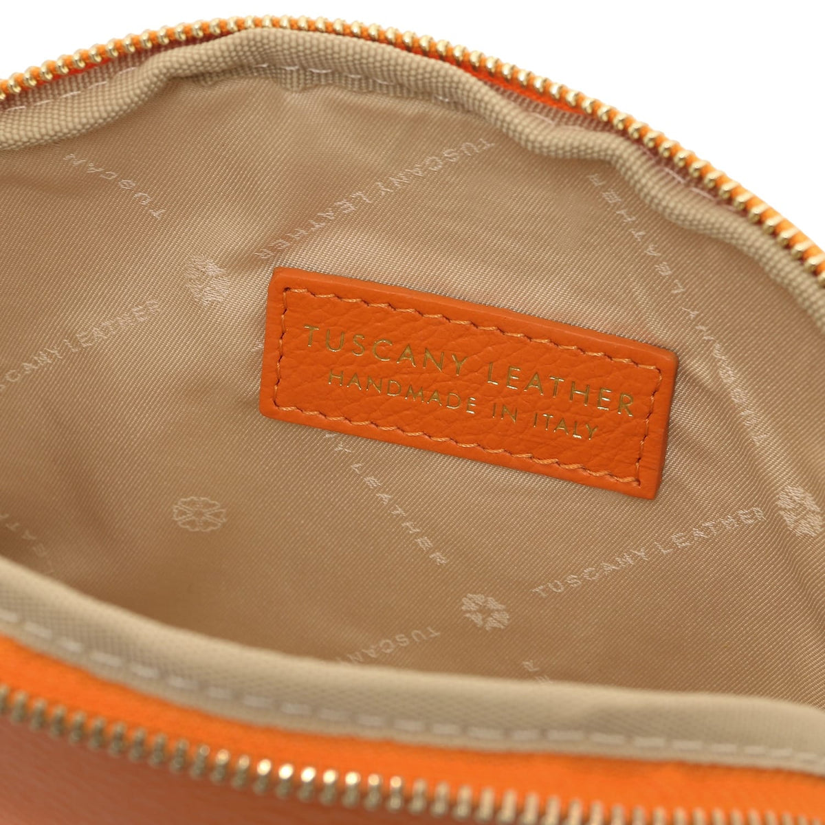 Primo piano of beige fabric fodera interna con embossed Tuscany Leather breing e stitched arancione leather label inside toiletry case.