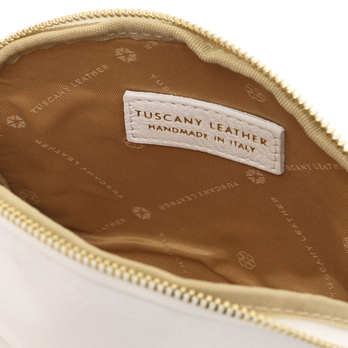 Primo piano of beige leather toiletry case interior featuring breed fodera in tessuto e stitched Tuscany Leather label inside zipper opening.