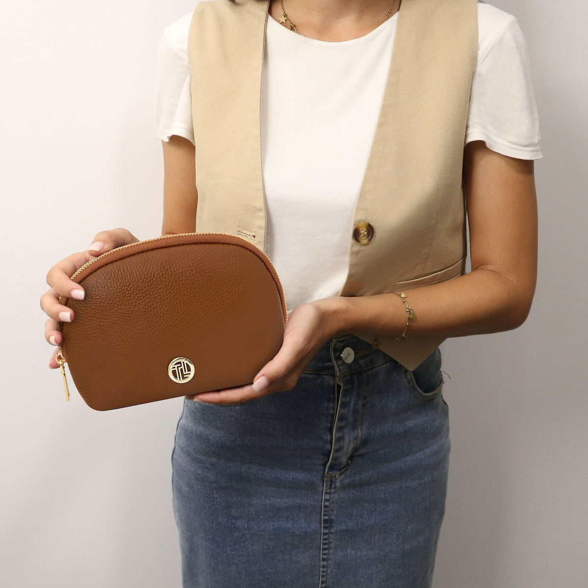 Rounded cuoio marrone pelle morbida toiletry case con zip color oro tenuta da una persona in a bianco top.