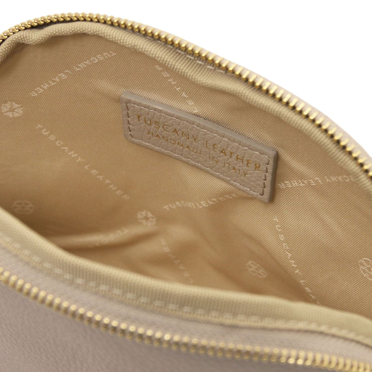 Primo piano of soft beige leather toiletry case interior featuring breed fodera in tessuto e leather label inside zipper opening.